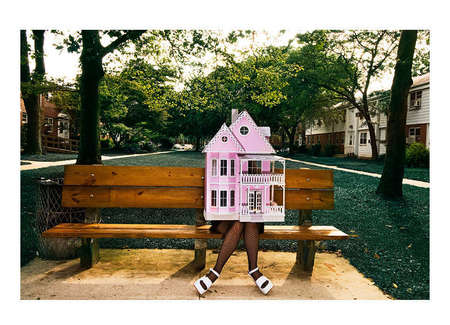 Artist Raven Schlossberg from a series on artists in New York wearing a doll house on bench at housing complex in Queens New York